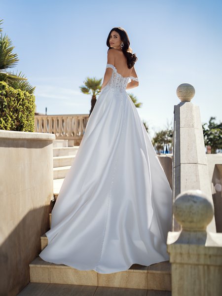 Radiating grace and sophistication, a bride in Moonlight Couture H1588 a Mikado wedding dress stands on the steps, her gown featuring a mesmerizing lace bodice, illusion back, and exquisite swag sleeves