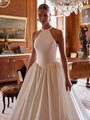 A bride in a stunning Mikado wedding dress, showcasing pleats at the Basque waist, stands gracefully in an elegant room Moonlight Couture H1602