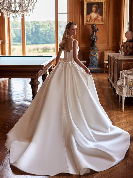 The back view of a bride in a luxurious Mikado wedding gown, adorned with pearls, exudes elegance in a refined setting.