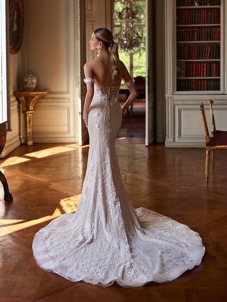 The back of a bride in a stunning illusion open back elaborately beaded wedding dress, poised in a beautifully adorned room