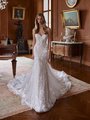  A bride stands in an opulent, vintage-style room wearing an elegant, strapless wedding gown with a fitted bodice and a sweetheart neckline. The dress features intricate lace detailing and floral appliqués, cascading down the gown