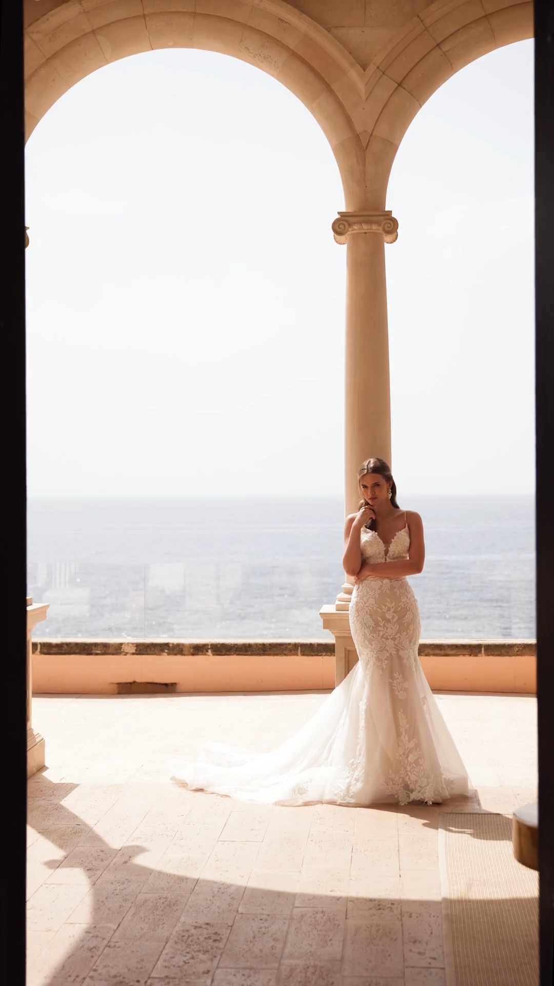 Bride standing next to column in classic lace wedding dress with bodice cutouts and sweetheart neckline with spaghetti straps